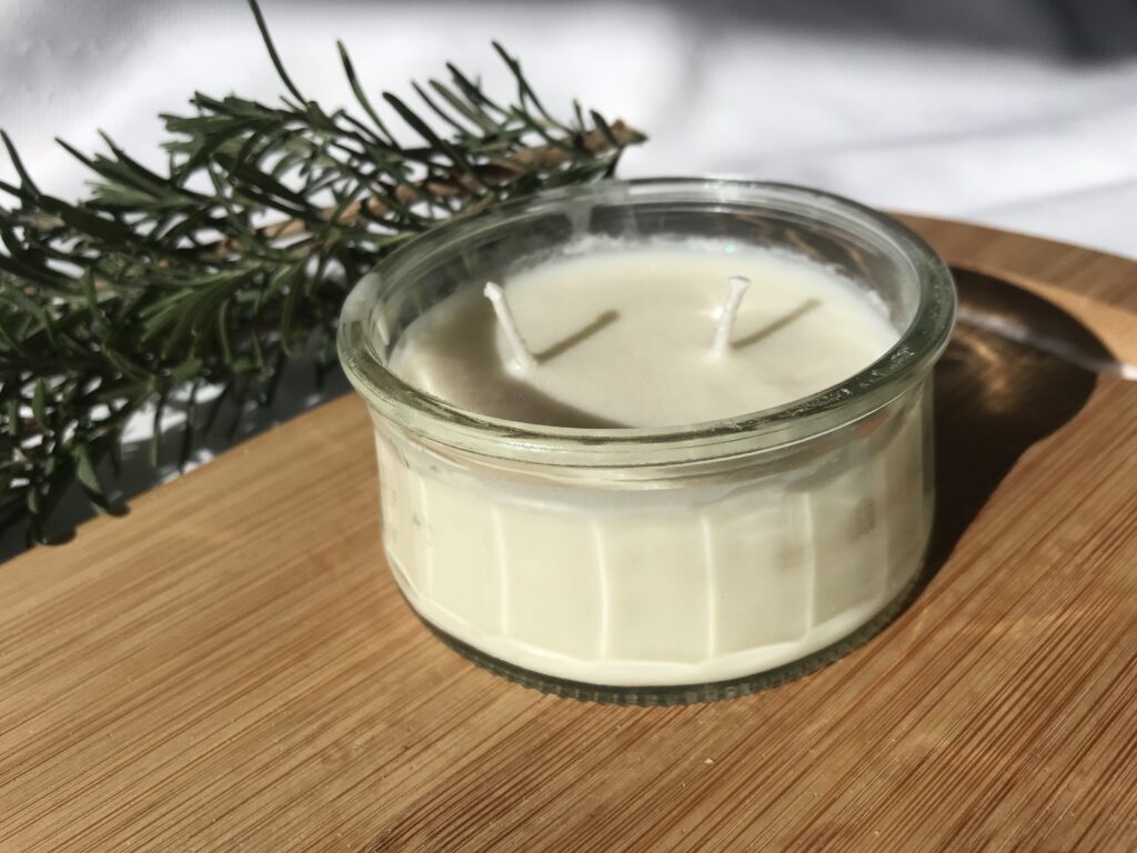 two wick, white soy candle on a cutting board, side by a piece of rosemary, on a white cloth.