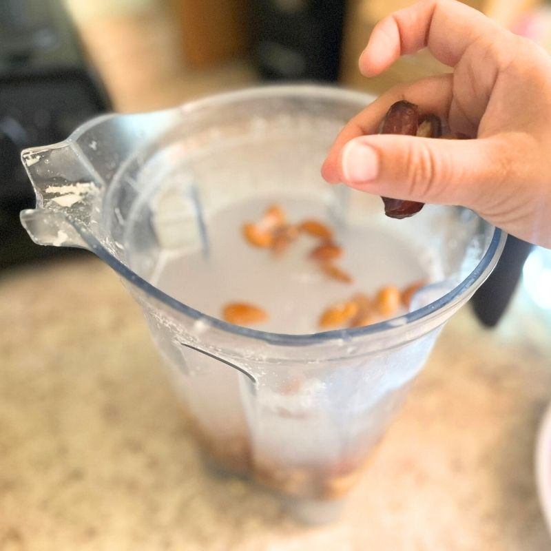 Almonds and dates being poured in the blender with water.