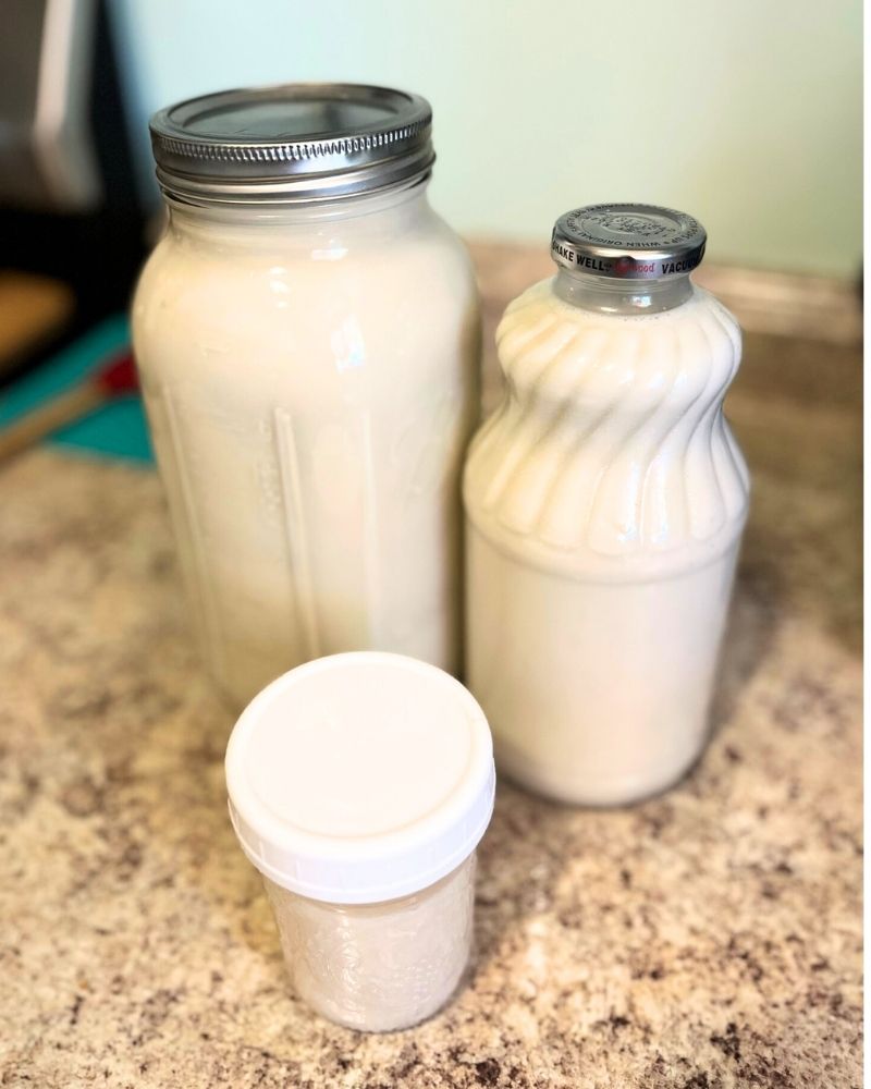 Three different sized glass jars with almond milk, sitting on a counter.