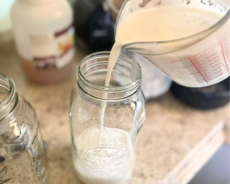 Fresh almond milk in a measuring cup being poured into a mason jar.
