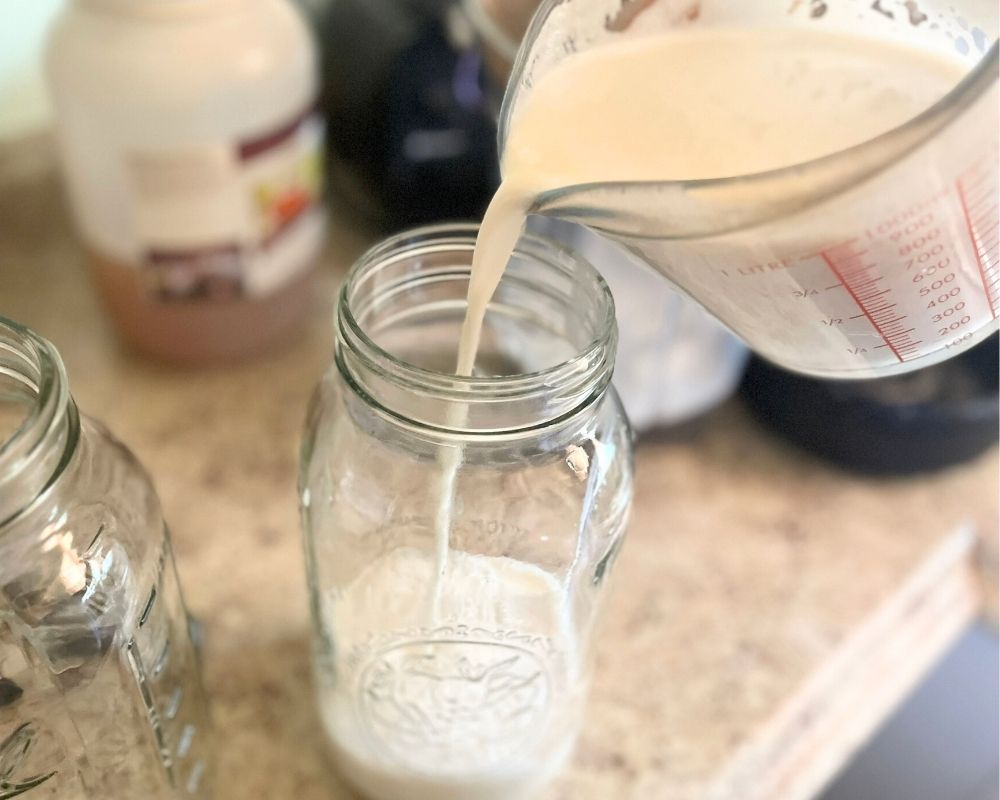 Fresh almond milk in a measuring cup being poured into a mason jar.