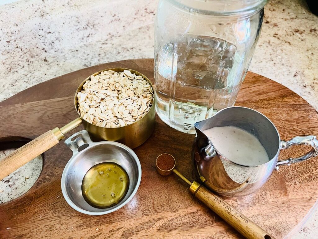 oats, water, honey, almond milk in containers on top of a brown cutting wood board.