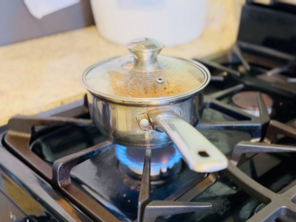 Small silver pot over stove top with fire on