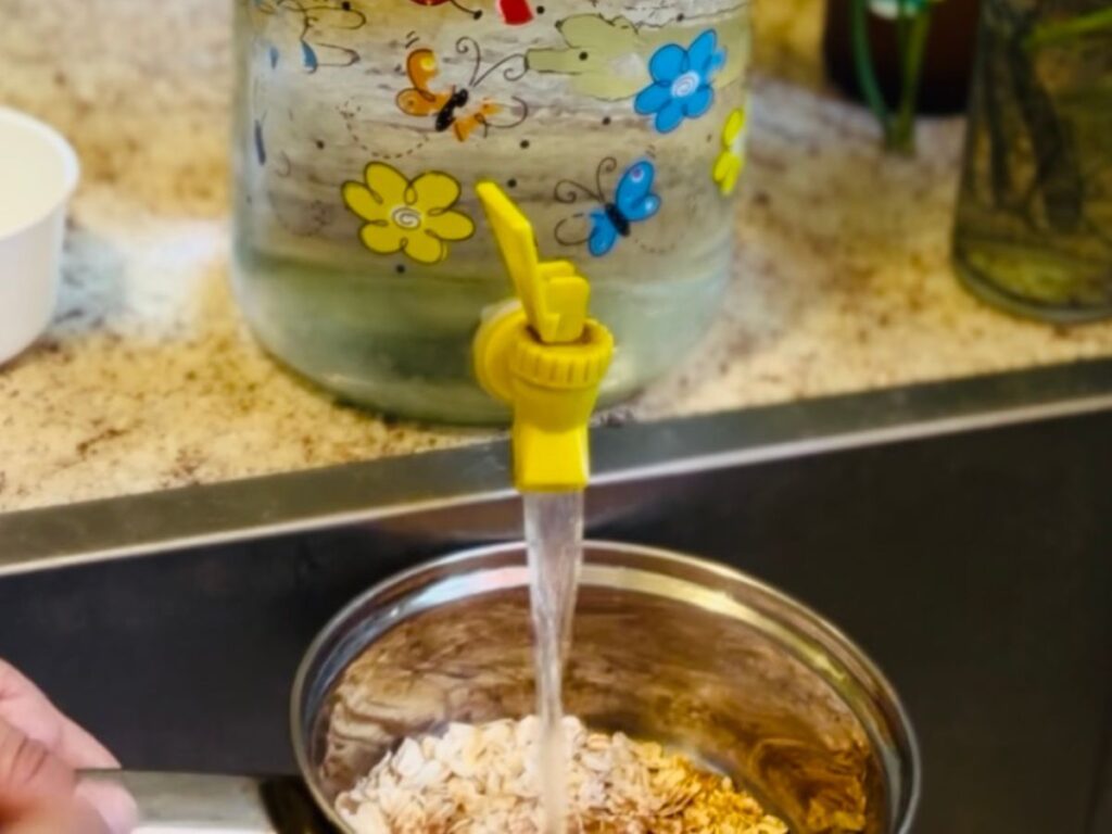 water container pouring water over oats in a small silver pot.