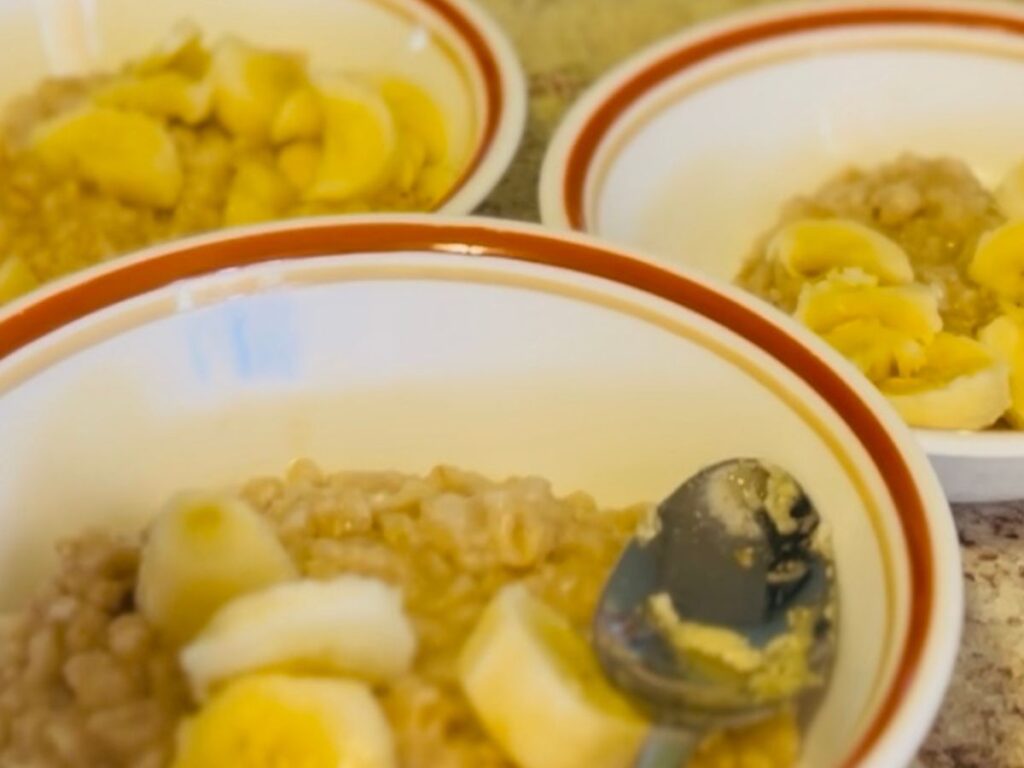 3 bowls with oatmeal and topped with chopped banana and a spoon on top.