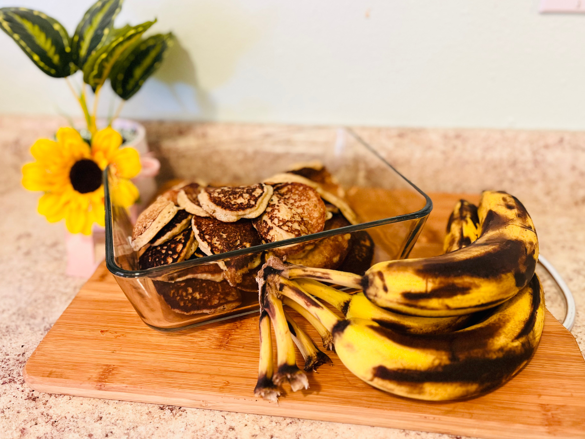 pancakes in a container with ripe bananas on the side on top of cutting board with a daisy on the side