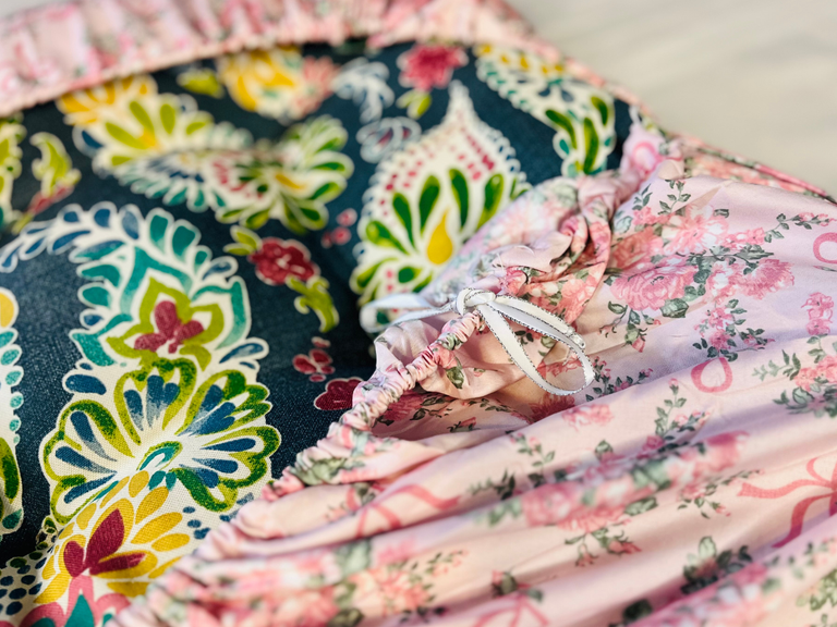 Blue floral cushion wrapped with a pink floral cover with a white ribbon tide to it.