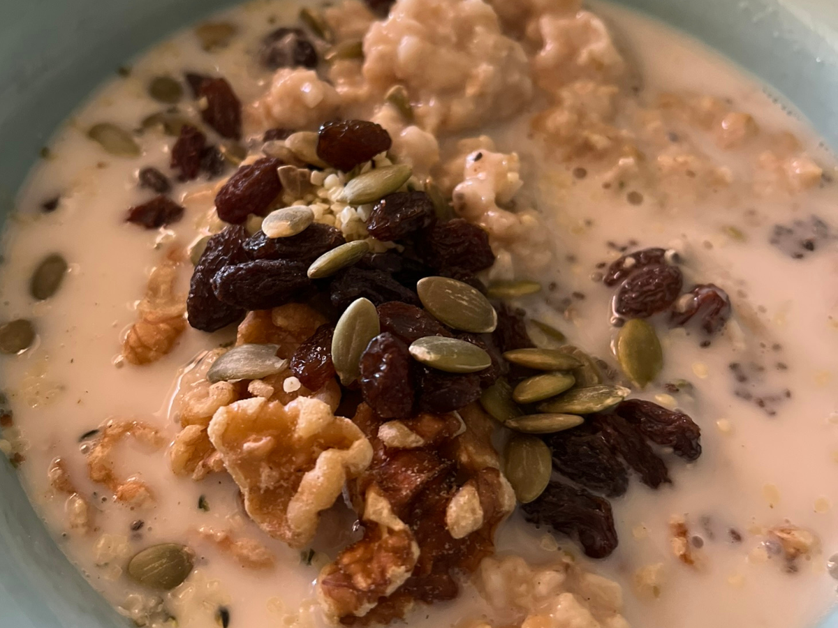 Oatmeal breakfast bowl served with almond milk and topped with raisins and seeds