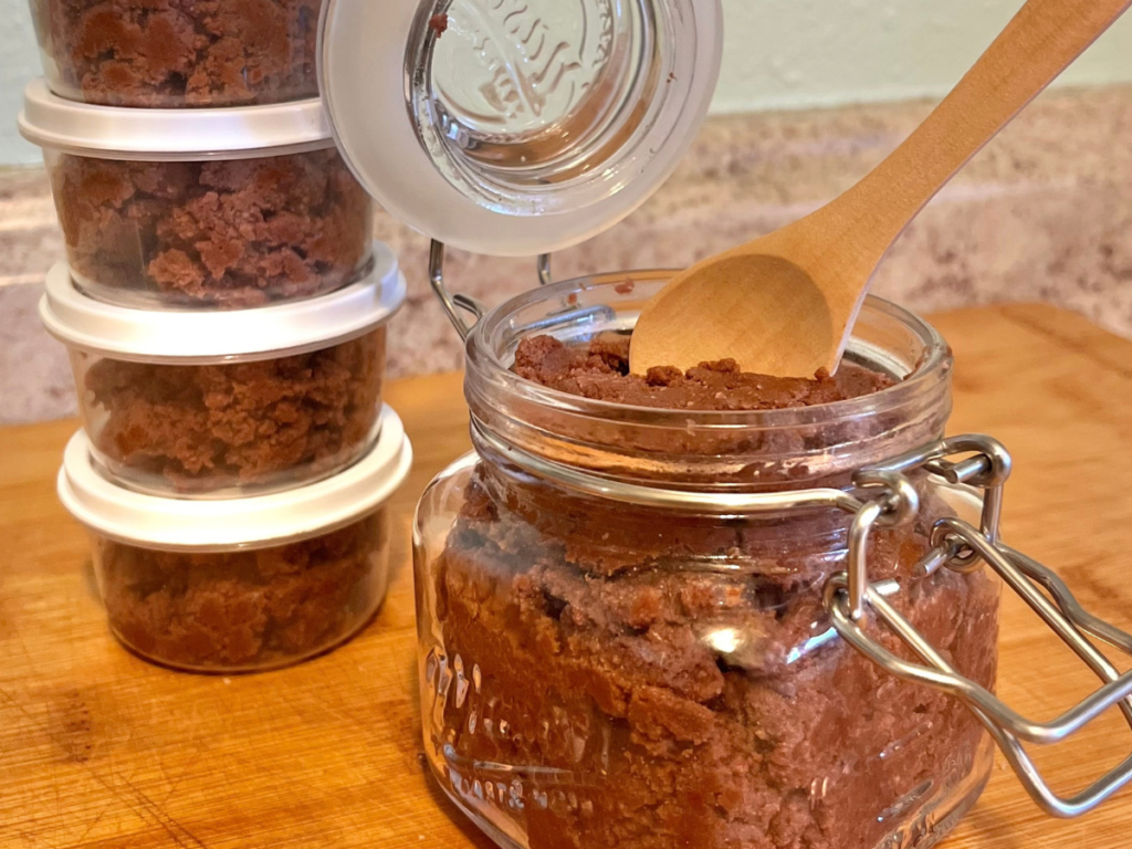 small containers filled with chocolate next to a chocolate glass container with a wooden spoon inside.