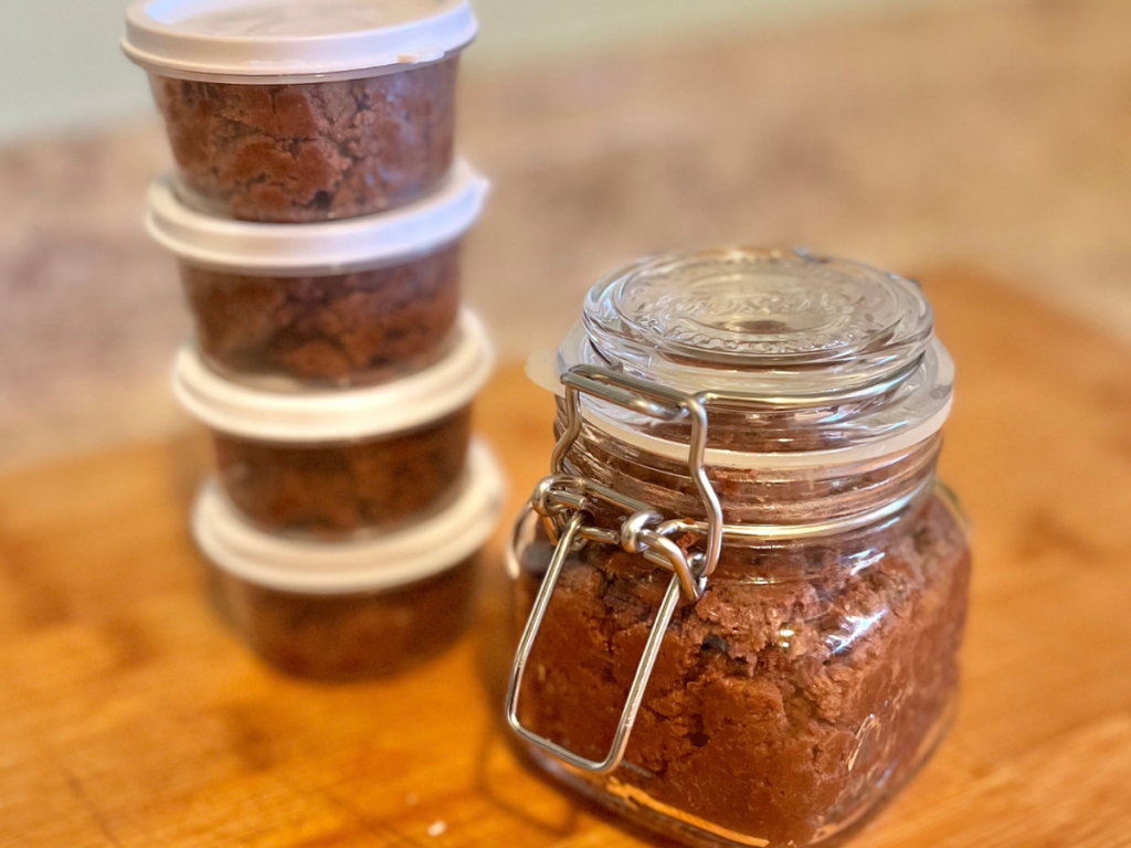 small containers filled with chocolate with a white lid next to a closed glass container also filled with chocolate spread.