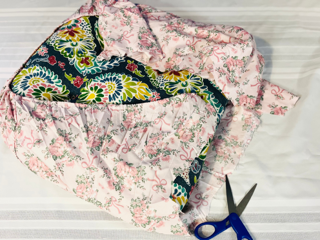 blue cushion wraped with w light pink floral fabric cut out with blue scissors by its side.
